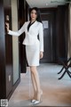 A woman in a white suit leaning against a door.