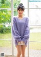 A woman standing in front of a window wearing a purple sweater.