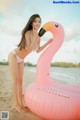 A woman in a white bikini standing next to a pink flamingo.