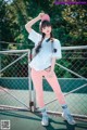 A woman in a white shirt and pink pants posing on a tennis court.