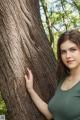 A woman leaning against a tree in the woods.