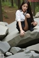 A young woman sitting on a rock in the woods.