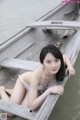 A woman in a white bikini sitting on a wooden boat.