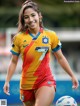 A woman in a yellow and red uniform holding a soccer ball.