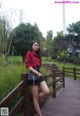 A woman in a red shirt and black shorts posing on a wooden bridge.