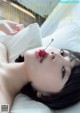 A woman laying in bed with a cherry in her mouth.